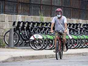 A cyclist wearing a mask rides past a row of Bike Share Toronto rental bikes during the COVID-19 pandemic on Monday, July 27, 2020.