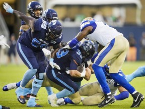 Toronto Argonauts running back Andrew Harris (centre) runs the ball with teammate Dejon Allen (left) against Winnipeg Blue Bombers defender Willie Jefferson (right) during the first half of a CFL game in Toronto on July 4, 2022.