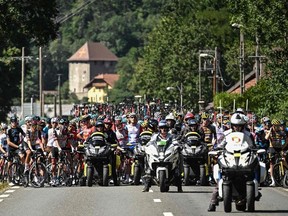 The pack of riders is temporarily immobilized by race regulators (front) due to protest action on the race route during the 10th stage of the 109th edition of the Tour de France cycling race, 148,1 km between Morzine and Megeve, in the French Alps, on July 12, 2022.