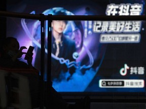 A man using his smartphone is silhouetted near an advertisement for Douyin, the Chinese sister app of TikTok, at a mall in Beijing, Aug. 30, 2020. A Chinese court in Sichuan province executed a man Saturday, July 23, 2022, who was convicted of homicide for setting his former wife on fire in September 2020 while she was livestreaming on Douyin.
