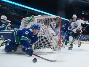Vancouver Canucks' Jake Virtanen (18) falls in front of Edmonton Oilers' Ethan Bear (74) as he reaches for the puck while Jesse Puljujarvi, right, watches during the first period of an NHL hockey game in Vancouver, on Saturday, March 13, 2021.