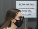 A pedestrian wearing a mask walks past Help Wanted signage at 