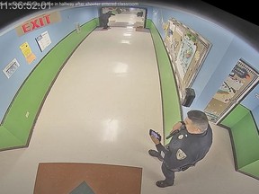 In this photo taken from surveillance video provided by the Uvalde Consolidated Independent School District via the Austin American-Statesman, shows officer Ruben Ruiz, whose wife, Eva Mireles was killed in the shooting, checking his phone in the hallway at Robb Elementary School in Uvalde, Texas, Tuesday, May 24, 2022.