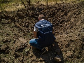 A war crime prosecutor kneels near a university facility in Mykolaiv, Ukraine, that was shelled on July 15.
