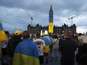 Die Parlamentsgebäude werden in den Farben der ukrainischen Flagge beleuchtet, wenn Menschen am 24. August 2022 auf dem Parliament Hill in Ottawa an den Feierlichkeiten zum ukrainischen Unabhängigkeitstag teilnehmen.
