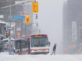 A pedestrian crosses the street as a city bus is pictured stuck during a winter storm in Toronto on Monday, Jan. 17, 2022.