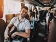 Young man relaxing in seat of bus amongst other happy travellers.