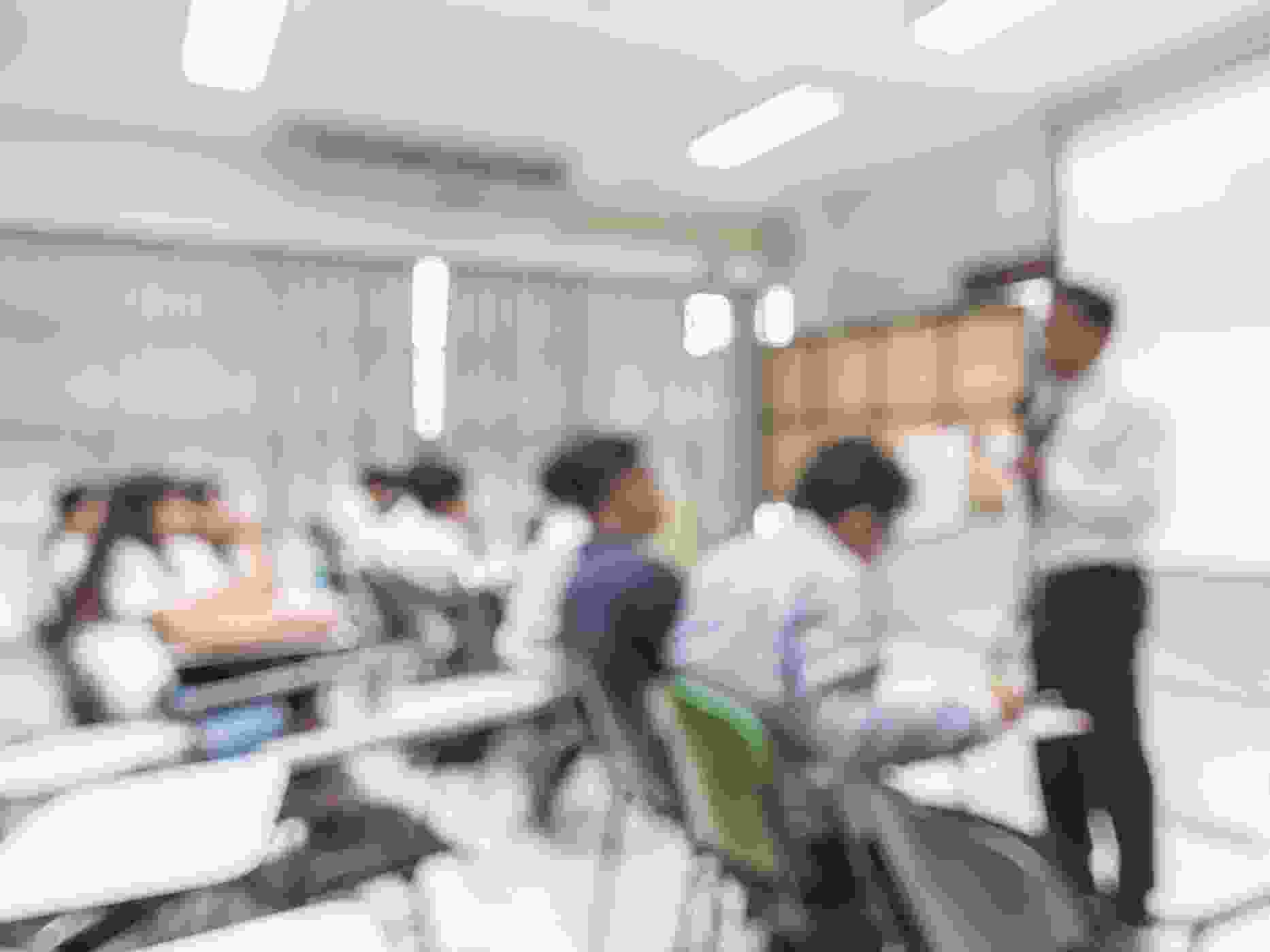 Blurred abstract background of students sitting in classroom with teacher in front of class.