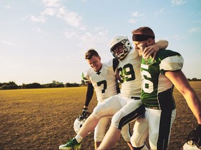 Football players carrying an injured teammate off the field during a practice session in the late afternoon.