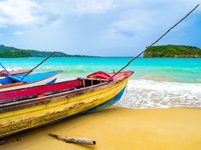 Colorful old wooden fishing boats docked by water on a beautiful beach coast. White sand sea shore landscape on tropical Caribbean island