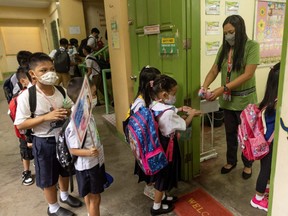 A teacher sprays alcohol on the hands of students for protection against COVID-19, on the first day of in-person classes at a public school in San Juan City, Philippines, Monday, Aug. 22, 2022.
