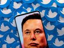In dieser Abbildung ist ein Bild von Elon Musk auf einem Smartphone zu sehen, das auf gedruckten Twitter-Logos platziert ist.  