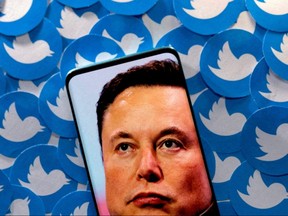 An image of Elon Musk is seen on a smartphone placed on printed Twitter logos in this picture illustration.