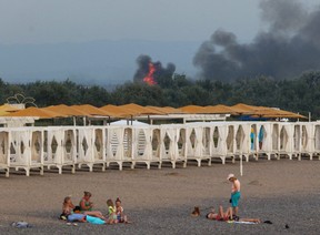 People rest on a beach as smoke and flames rise after explosions at a Russian military airbase, in Novofedorivka, Crimea, Aug. 9, 2022.