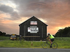 A bicyclist rides past a barn with political banner on it as the sun rises on primary election day, Tuesday, Aug. 9, 2022, in Suffield, Conn. Suffield is one of several small towns in Connecticut where control was flipped from Democrats to Republicans in 2021 municipal races.