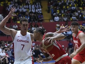 Panama's Trevor Gaskins, centre, dribbles the ball against Canada's Dwight Powell, left, during a basketball WCup America's qualifying match at the Roberto Duran arena in Panama City, Monday, Aug. 29, 2022.