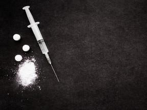 Powder, tablets and syringe on dark black table.