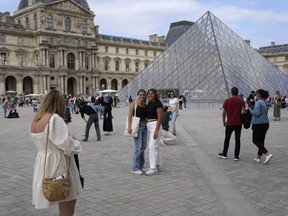 Tourists take pictures in front of the Pyramide in the Louvre Museum courtyard, in Paris, Monday, June 20, 2022.