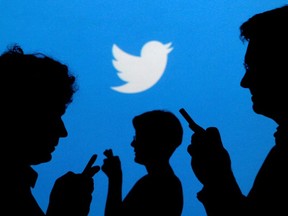 People holding mobile phones are silhouetted against a backdrop projected with the Twitter logo in this illustration picture taken September 27, 2013.