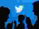 People holding mobile phones are silhouetted against a backdrop projected with the Twitter logo in this illustration picture taken Sept. 27, 2013. 