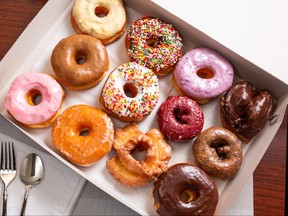 A top down view of a dozen assorted donuts in a box, in a kitchen setting.