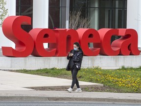 A pedestrian wearing a mask walks past Seneca College signage in Scarborough on May 5, 2021.