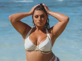 Model Ella Halikas wearing a white bikini, posing in ocean with arms on head.