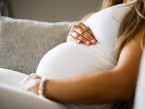 Close-up of pregnant woman relaxing and sitting on the side on the sofa.