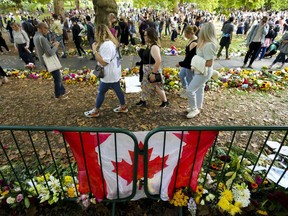 Long lines of mourners form and lay flowers near a Canadian flag as people wait to pay their respect near the gates of Buckingham Palace in London on Sunday, Sept. 11, 2022.