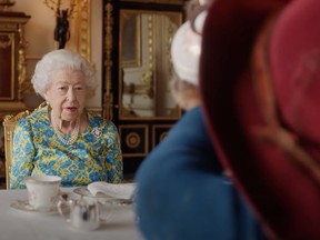 Queen Elizabeth watches as Paddington Bear drinks from teapot in Buckingham Palace.