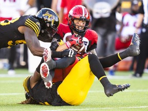 Calgary Stampeders quarterback Bo Levi Mitchell gets sacked by Hamilton Tiger-Cats' Tunde Adeleke, bottom, as Malik Carney, left, comes in on the play during first half CFL football action in Hamilton, Ont., Saturday, June 18, 2022.