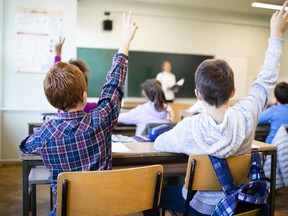 Schoolchildren at classroom with raised hands answering teacher's question.