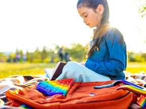 Young student reading book with backpack with rainbow straps next to her