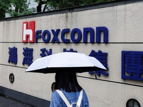 A woman carrying an umbrella walks past the logo of Foxconn outside a company's building in Taipei, Taiwan October 31, 2022.