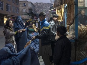 A man distributes bread to Burka-wearing Afghan women outside a bakery in Kabul, Afghanistan, Thursday, Dec, 2, 2021.