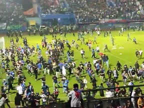 In diesem Screenshot aus den sozialen Medien rennen Fans am Samstag, den 1. Oktober 2022, auf ein Fußballfeld in Indonesien.