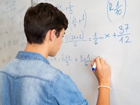 A student solves a math problem on whiteboard in a classroom.