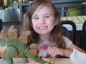 Little girl smiling for camera while playing with a toy dinosaur.