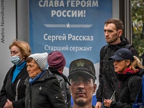 In this file photo, pedestrians walk past a poster displaying a Russian soldier with a slogan reading "Glory to the Heroes of Russia" decorating a bus stop in central Moscow on Oct. 12, 2022.