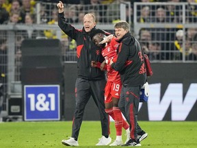 Bayern's Alphonso Davies, center, leaves the field after getting injured during the German Bundesliga soccer match between Borussia Dortmund and Bayern Munich in Dortmund, Germany, Oct. 8, 2022.