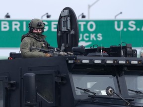 An Ontario Provincial Police tactical officer looks on from the top hatch of an armoured vehicle as demonstrators prepare to leave in advance of police enforcing an injunction against their demonstration, which has blocked traffic across the Ambassador Bridge by protesters against COVID-19 restrictions, in Windsor, Ont., Saturday, Feb. 12, 2022.