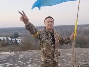 A man in military clothing gestures next to a Ukrainian flag in Kalynivske in Kherson region, Ukraine, Wednesday, Nov. 9, 2022 in this screen grab taken from a video.