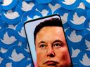 An image of Elon Musk is seen on a smartphone placed on printed Twitter logos in this picture illustration taken April 28, 2022.