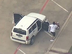 Screen shot of man holding a baby in a car seat exiting vehicle involved in police chase.
