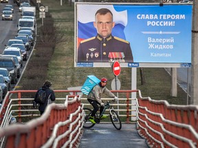 A courier rides past a public poster showing a Russian officer with the slogan "Glory to Russia's heroes" displayed in Saint Petersburg on November 18, 2022.
