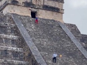 Woman at top of Mayan pyramid while a security guard climbs up to escort her down.
