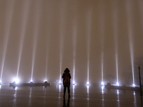 A lone woman braves the rain to take a moment in silence as the sky is lit with 14 beams of white light during ceremonies to mark the anniversary of the massacre at Ecole Polytechnique in Montreal, on Tuesday, Dec. 6, 2022.