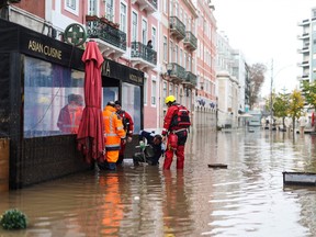 Firefighters try to open a drain along a flooded street following heavy rains in Lisbon on December 13, 2022.