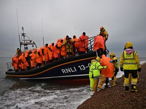 In this file photo taken on December 9, 2022 migrants, picked up at sea attempting to cross the English Channel, are helped ashore from an Royal National Lifeboat Institution (RNLI) lifeboat, at Dungeness on the southeast coast of England.