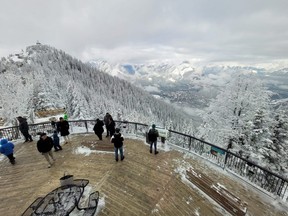 Visitors take in the view from an outdoor observation area at the upper terminal of the Banff Gondola in Banff, Alta.